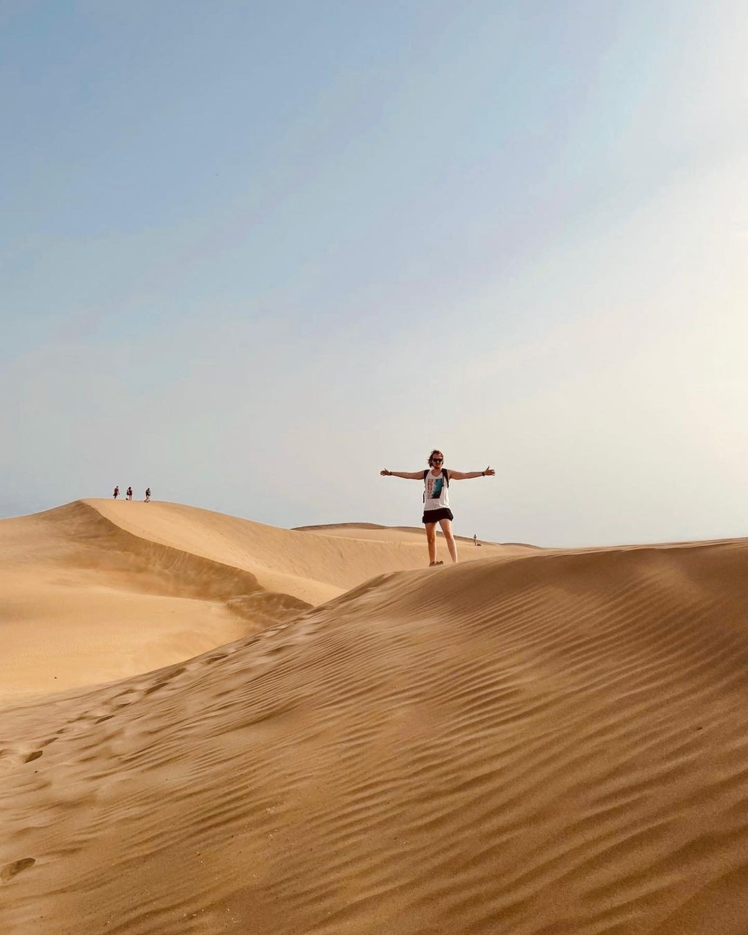 Elvis Baltais standing on sand dunes with arms outstretched